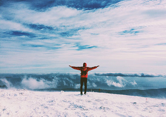 A person stands on the edge of a glacier and looks out at snowy mountain tops