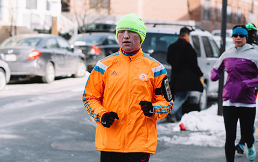 A man wearing a Boston Marathon jacket runs during the winter