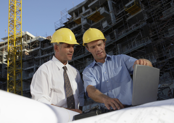 Two men use a laptop on a construction site