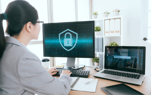 Woman working on a computer and laptop with cybersecurity software.