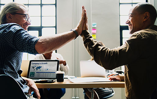 Two IT pros high five because they completed a job with knowledge from CompTIA