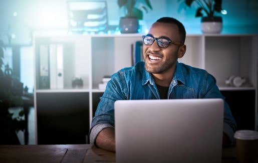 Man working on a computer, wearing glasses, smiling into the distance.