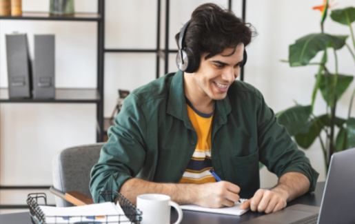 Male smiling and wearing headphones taking notes from laptop