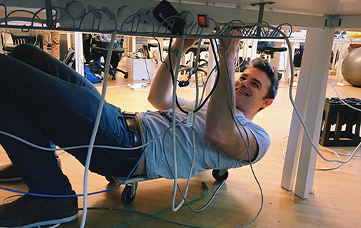 A help desk technician works with cords under a workstation