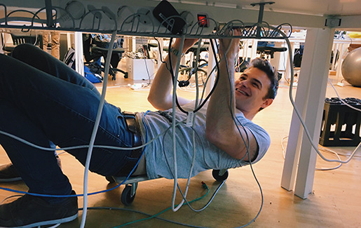 help desk technician A help desk technician works with cords under a workstation