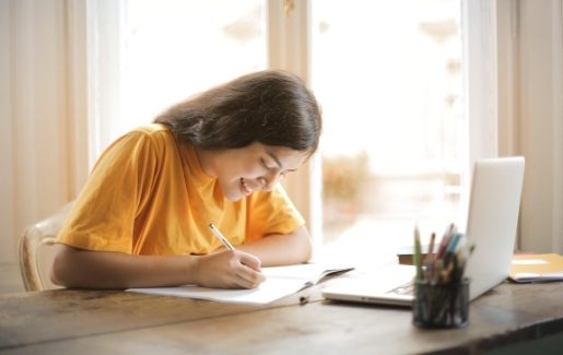 Young girl wearing a yellow shirt writing on notebook