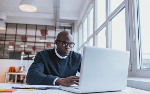 Male with glasses looking at laptop screen next to window during the day