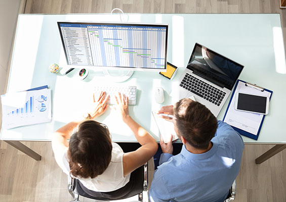 Two IT pros look at a Gantt chart while managing a project