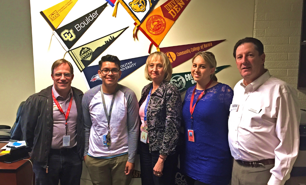 Jose Rivera and four of his teachers stand in front of a display of college banners.