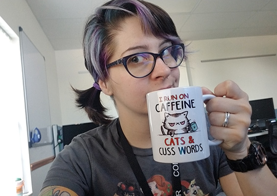 Molly Stewart holding a coffee mug that says, 'I run on caffeine, cats and cuss words.' 