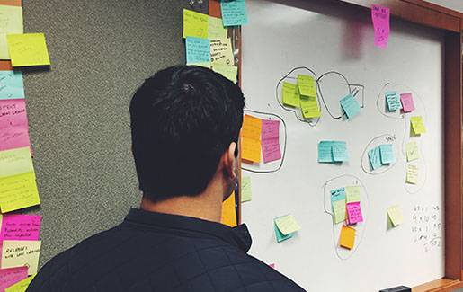 A cybersecurity professional looks at a whiteboard with sticky notes during project management