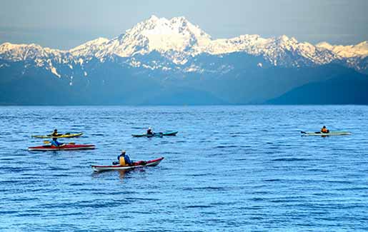 People kayak in Puget Sound in Seattle, looking at Olympic Mountains