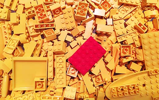 A red Lego in a pile of yellow Legos