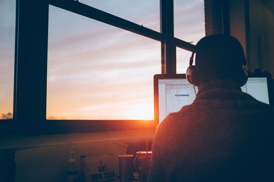 Man working on computer with setting sun behind.
