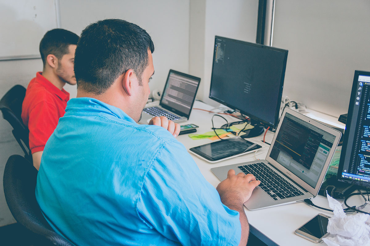 Security+ de CompTIA es una certificación global que valida las habilidades básicas que usted necesita para realizar las principales tareas de seguridad y seguir una carrera en seguridad de TI. Dos personas mirando muchos monitores.