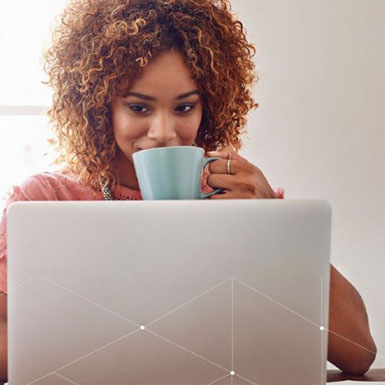 Woman drinks coffee and reads laptop.