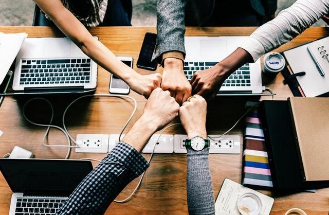 five hands fist bumping over laptops connected via an ad hoc network