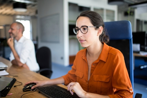 Woman in orange shirt and glasses looking at her computer in an office.