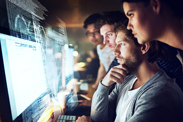 A cybersecurity team reviews information on a monitor while working on a project